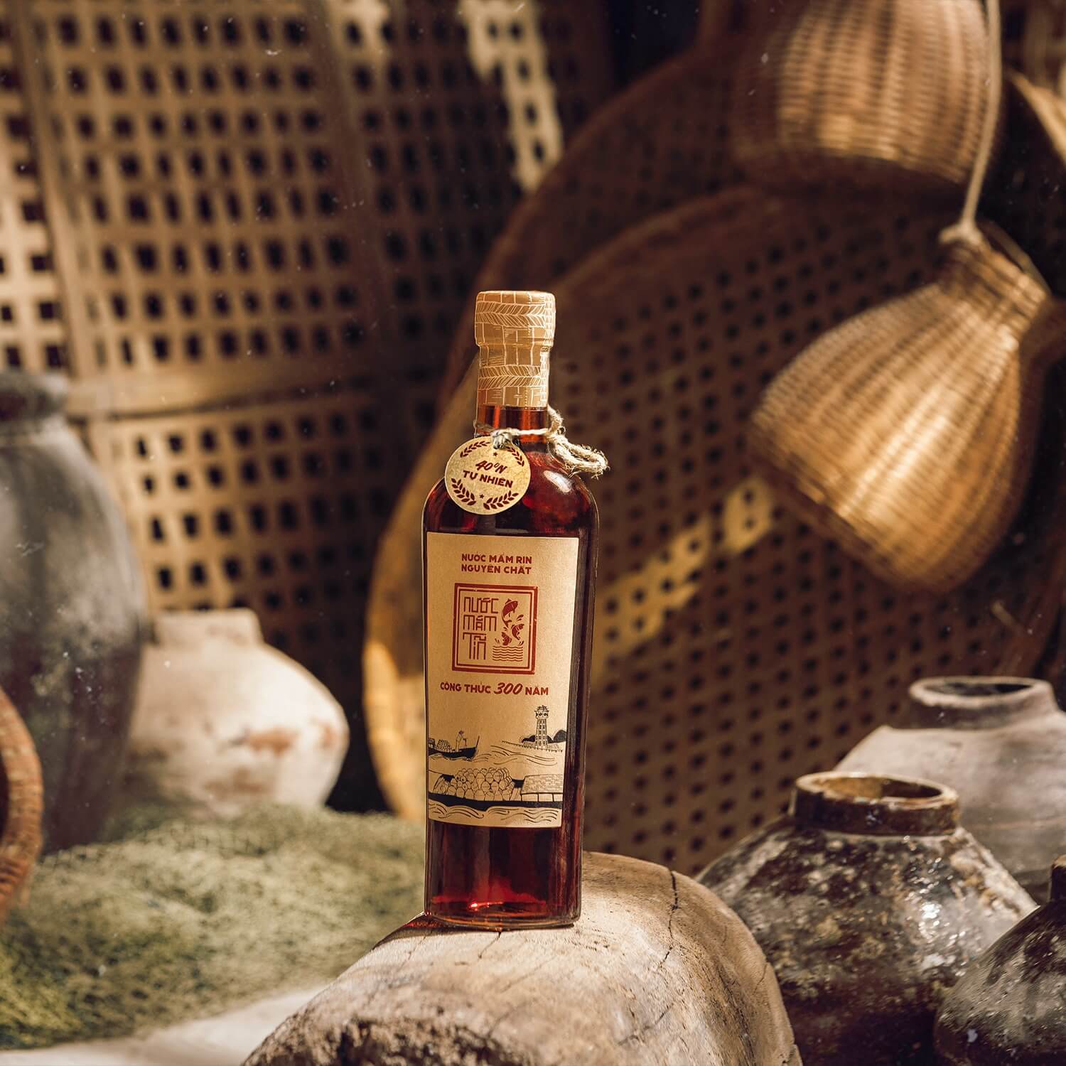 Chai nước mắm Tĩn nhãn đỏ đặt cạnh tĩn gốm và nong tre